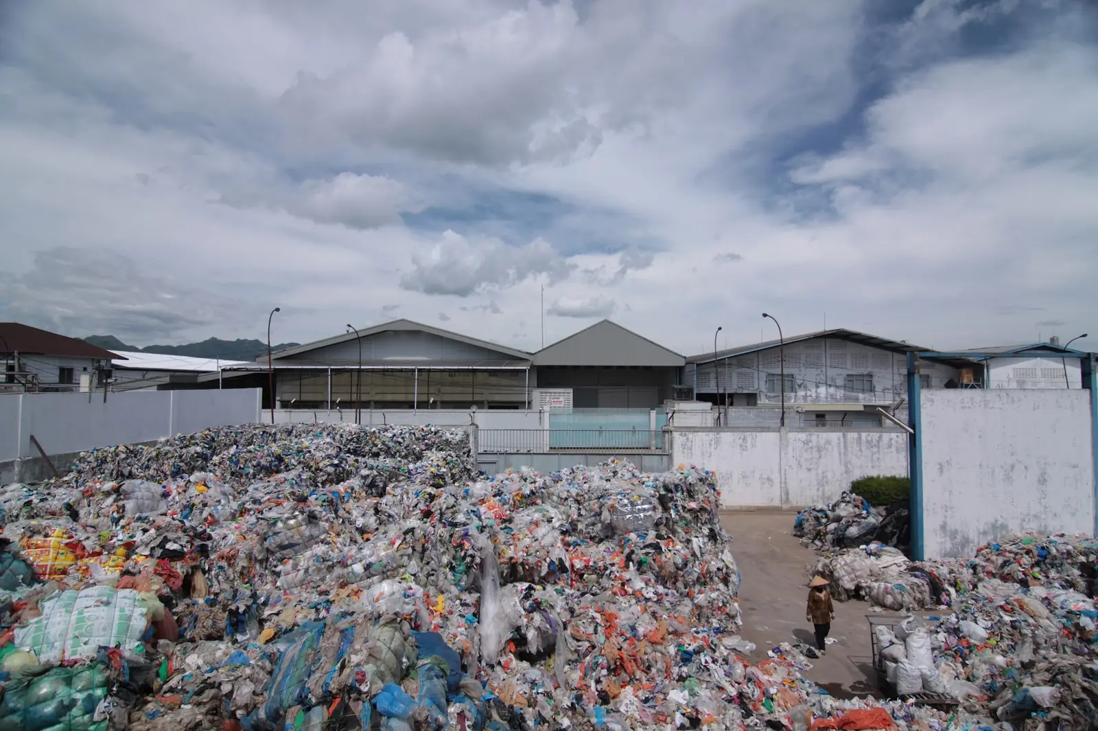 Halaman pabrik daur ulang dengan tumpukan plastik bekas di bawah langit berawan